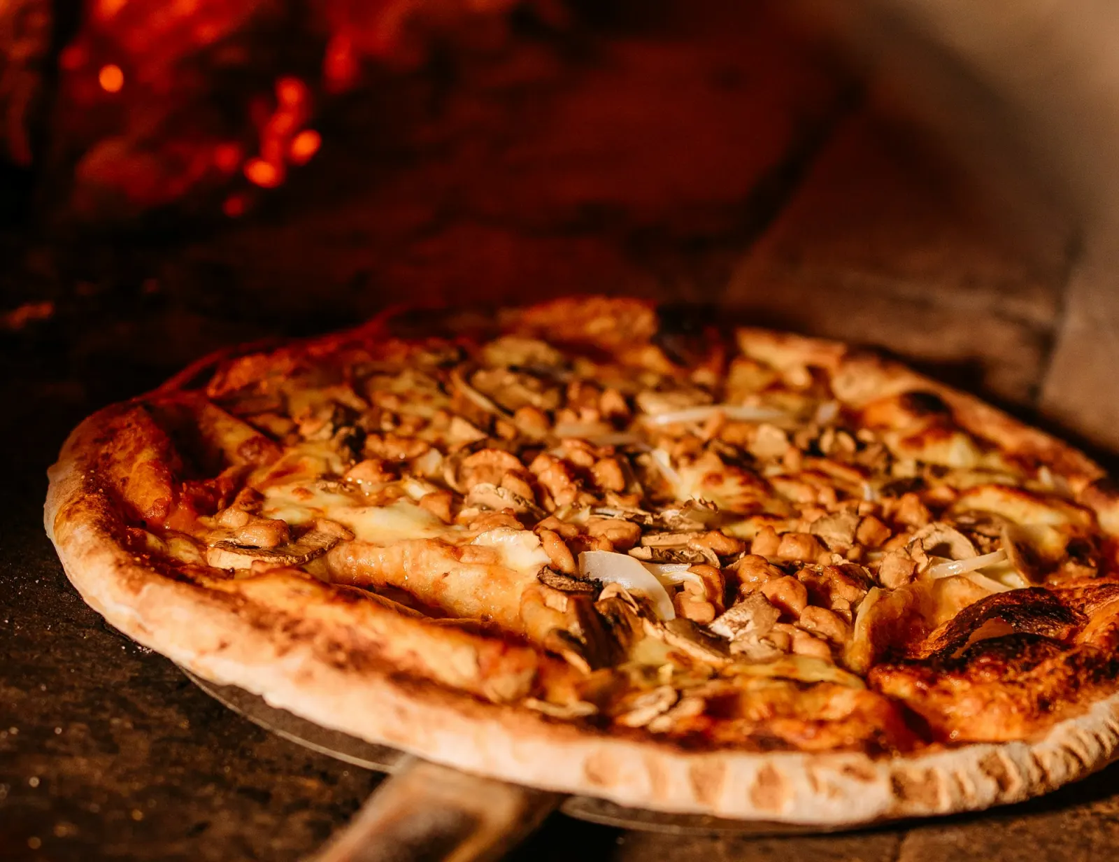 Pizza auf dem Holzschieber vor der Glut im Steinofen